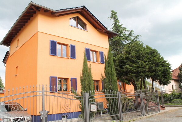 A two-story building with a flat roof, multiple windows with shutters, and a metal fence in front. - Seaside Villa Leipzig (Leipzig)