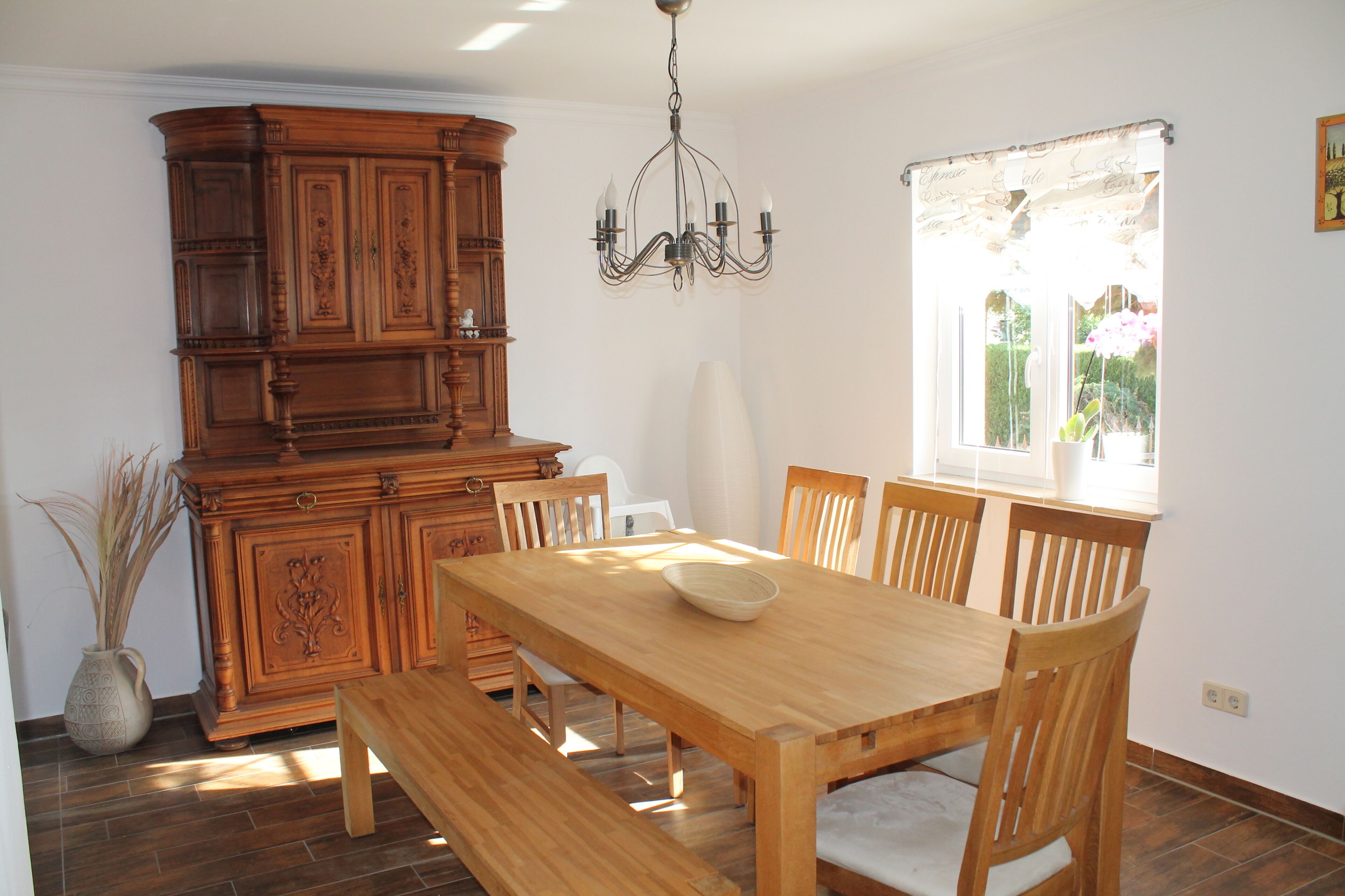 A dining area with a wooden table and benches, a chandelier, and a cabinet with decorative carvings.