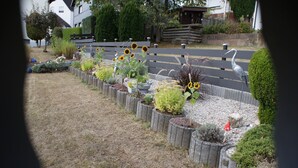 A garden with various plants and flowers, a wooden bench, and a road in the background. - Wonderful view of the Nahe Valley and the Frombork (Sonnenberg-Winnenberg)