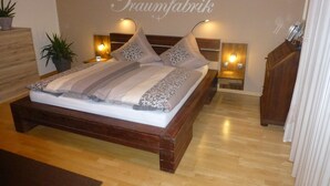 A bedroom with a wooden bed, decorative pillows, bedside lamps, and a wall with the text "Traumfabrik". - Wonderful view of the Nahe Valley and the Frombork (Sonnenberg-Winnenberg)