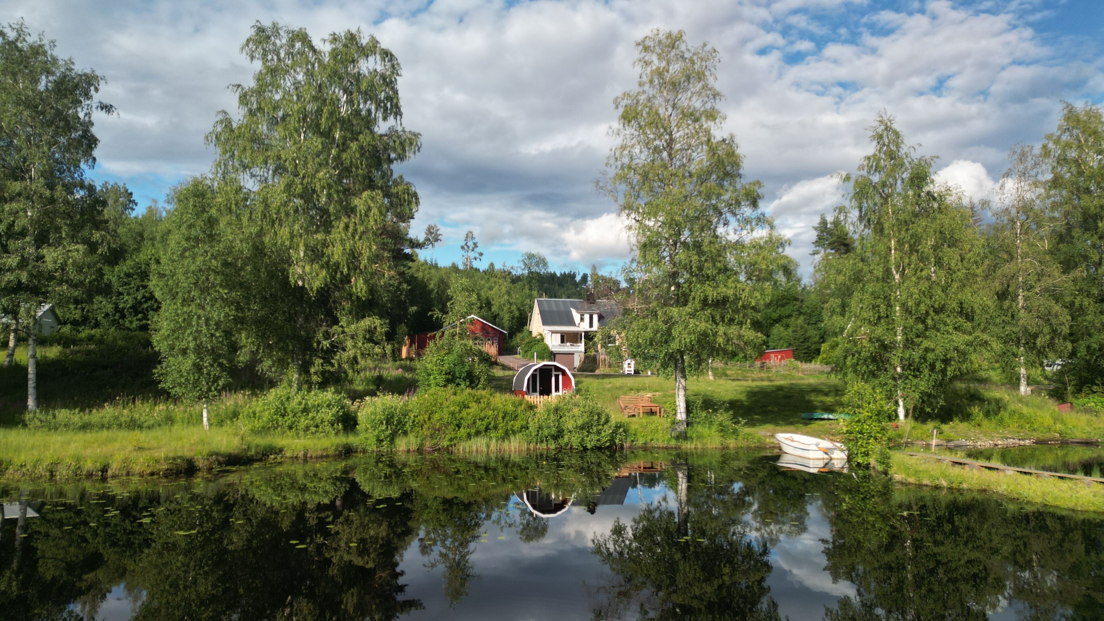 A lakeside property with a house, a red barn, and a boat docked by the water.