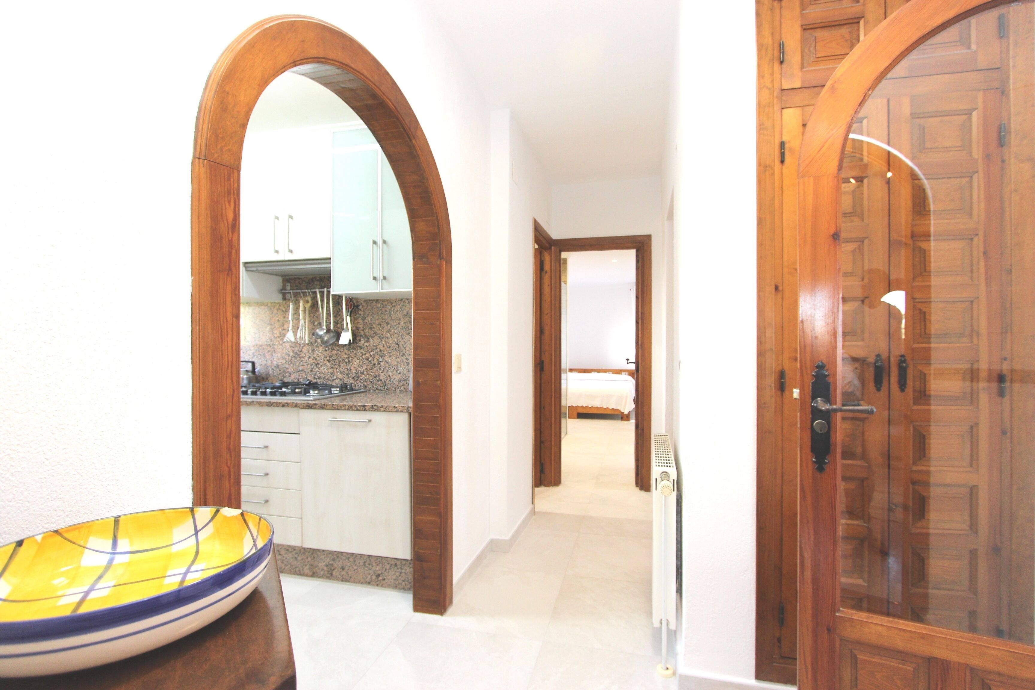 A hallway with wooden doors, a kitchen area with cabinets, and a bed in the background.