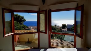 Quarto com vista de canto para uma varanda com vista da orla marítima.