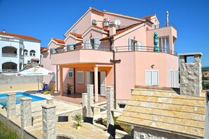 A two-story building with a swimming pool, outdoor seating, and a stone staircase.