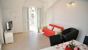 Ein modernes Zimmer mit Fernseher, einem roten Sofa, einem Esstisch mit blumigem Tischläufer und einem Balkon mit Blick.