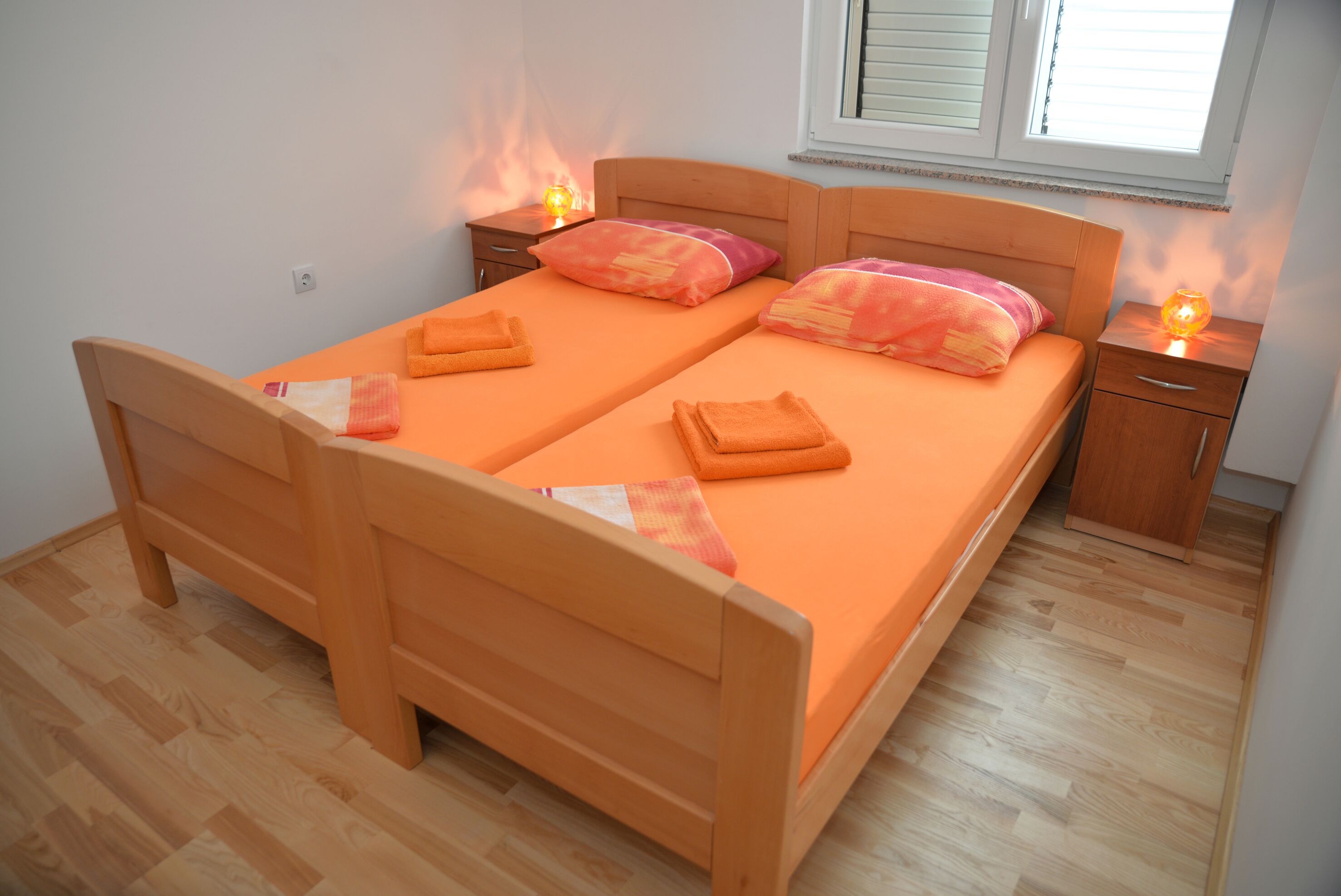 A double bed with orange bedding, two bedside tables with lamps, and a window with blinds.