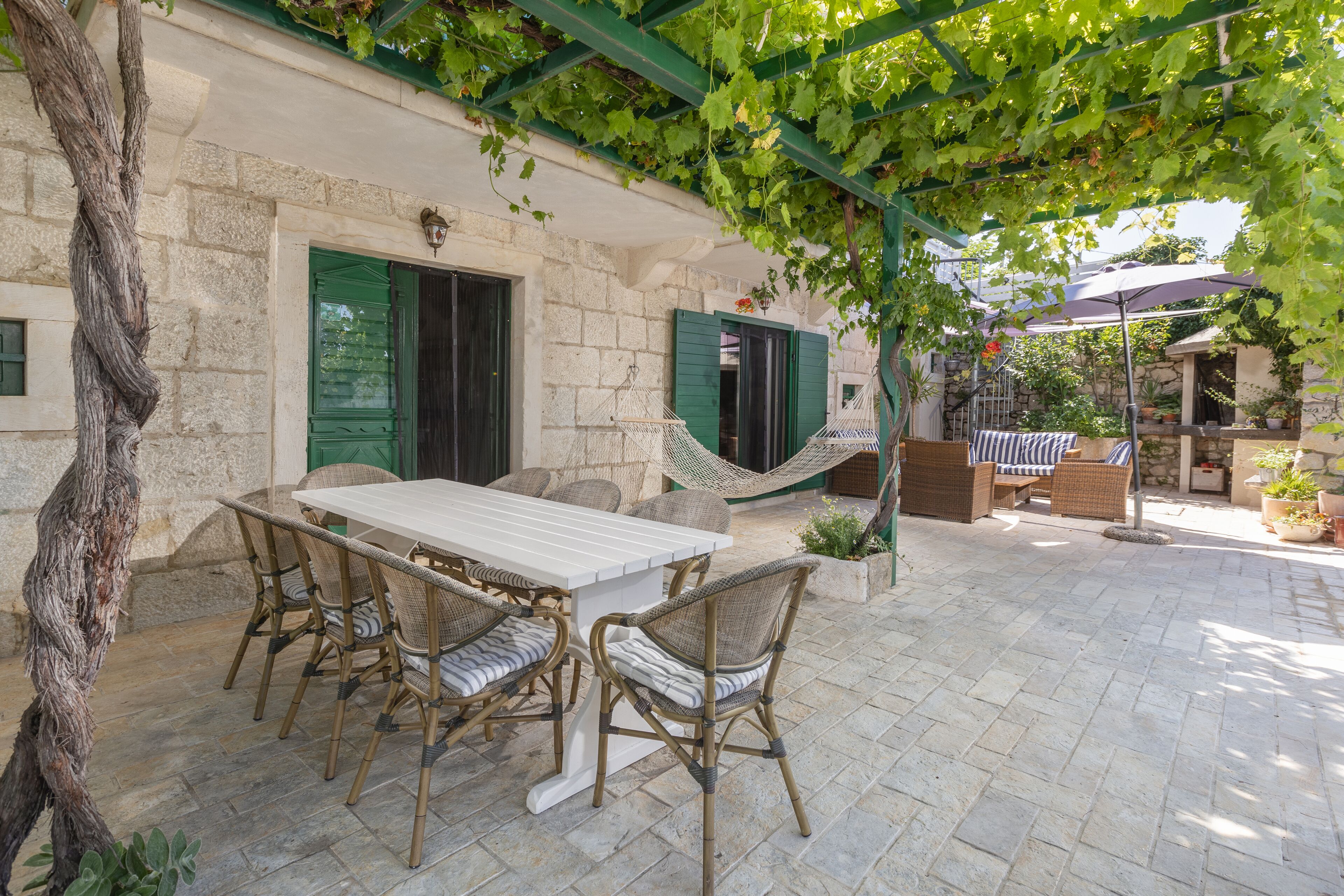 Une terrasse extérieure avec un sol en pierre, une table blanche, des chaises en osier et un hamac.