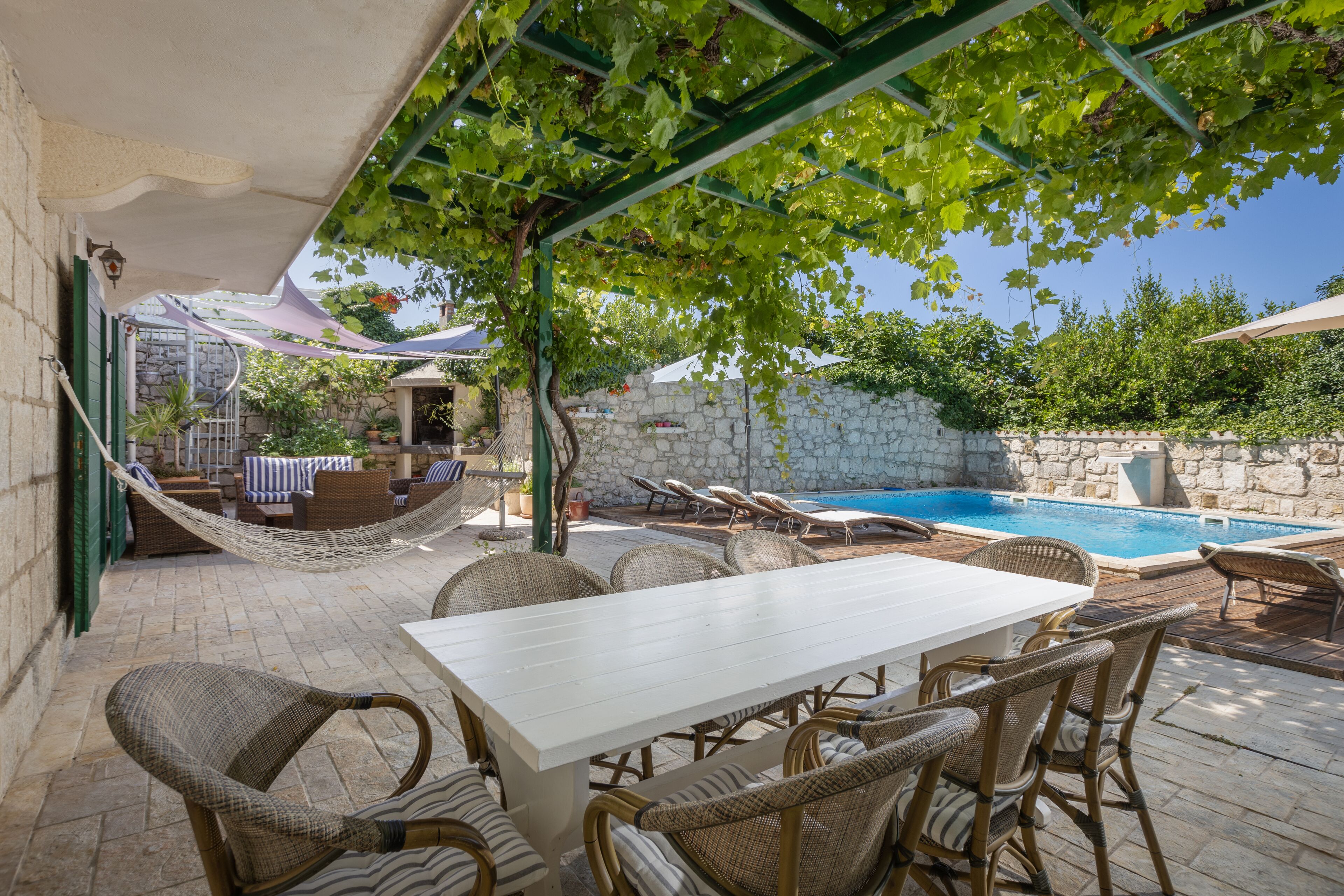 Un patio exterior con piscina, mobiliario de mimbre y una pared de piedra.