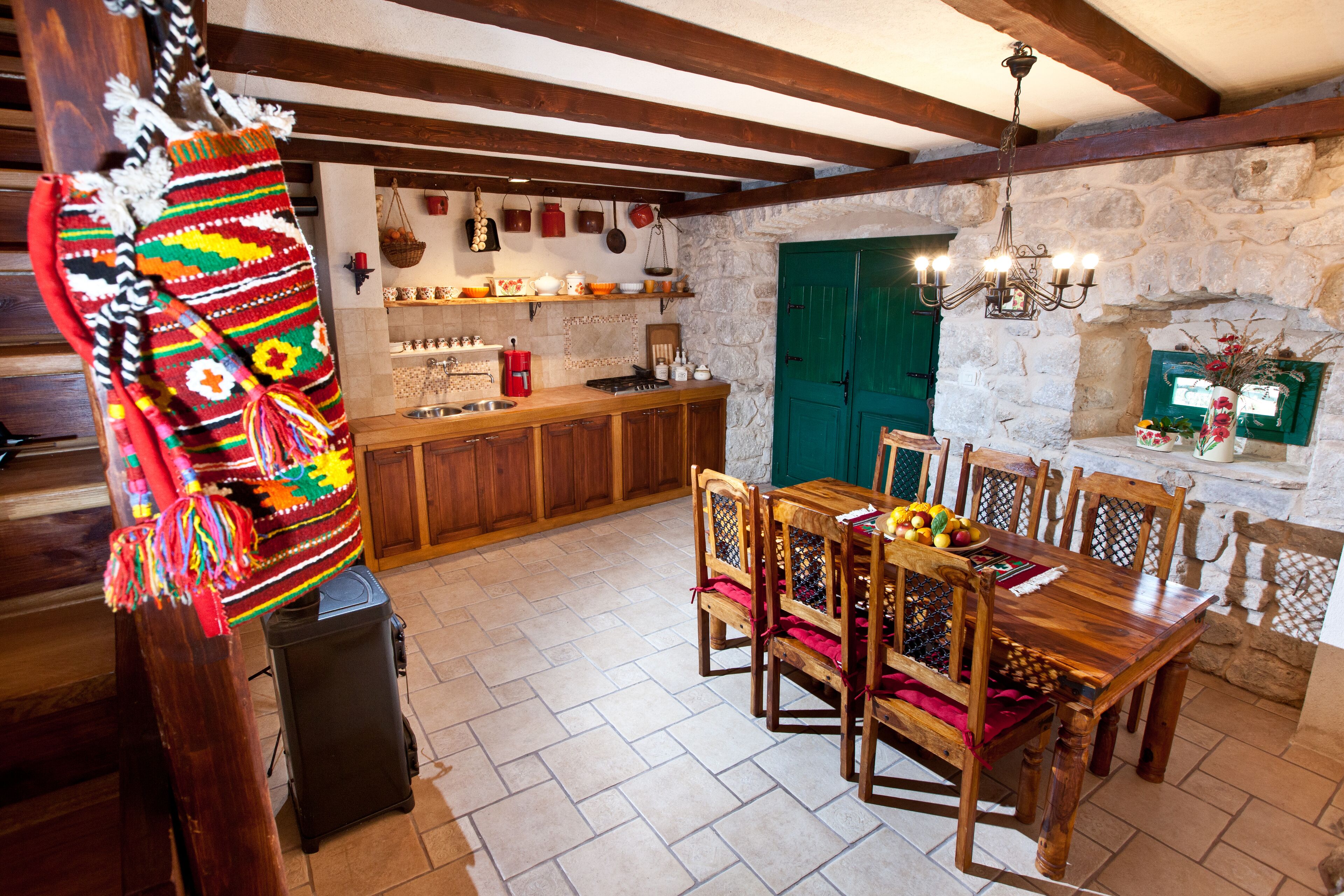 A rustic kitchen with wooden cabinets, a dining table with chairs, and a stone wall.