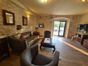 A living room with stone walls, a leather sofa, a grey armchair, a wooden coffee table, and a television. - Last minute for June - romantic villa with pool and BBQ, 6 min from the sea (Podgora)