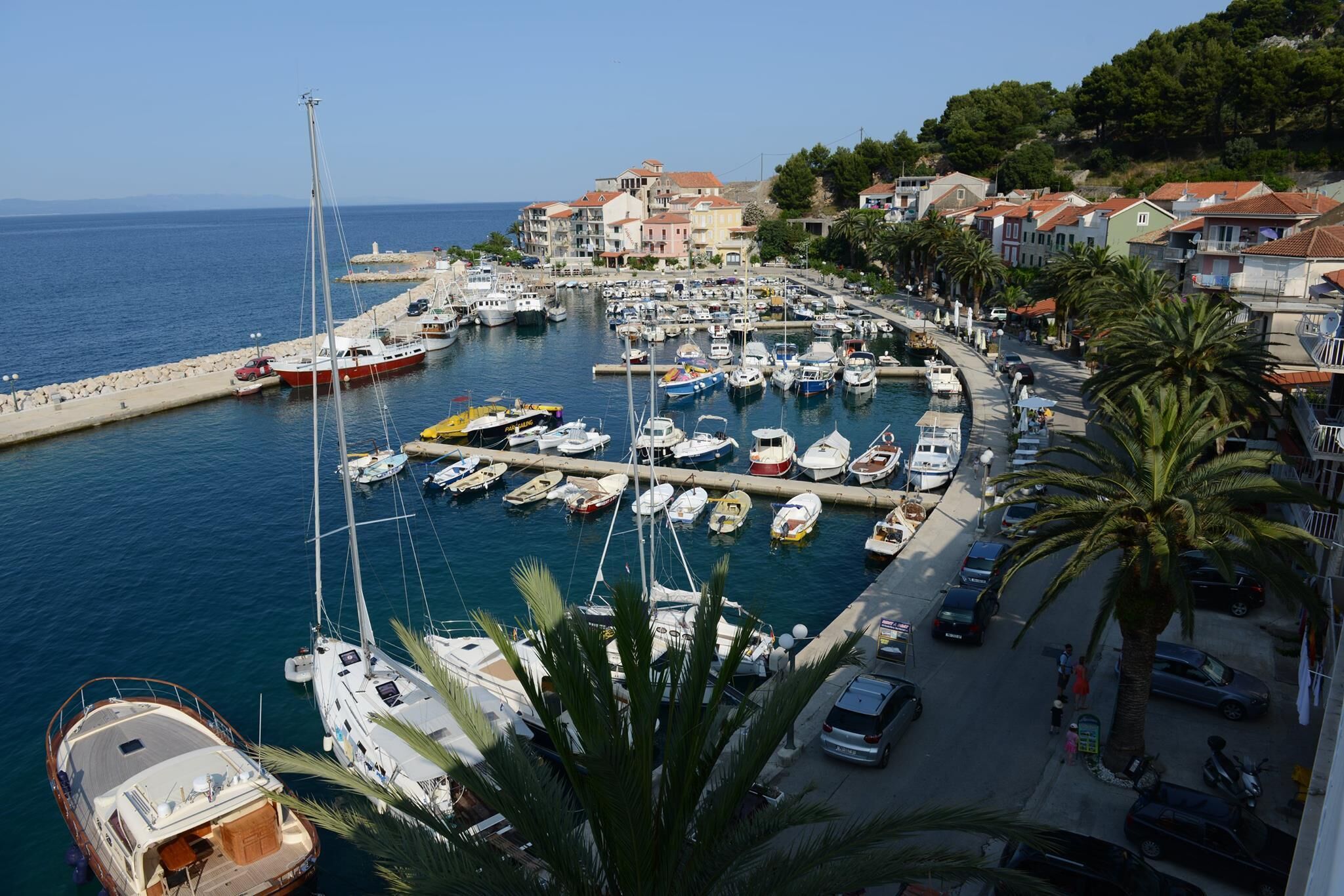 A marina with boats docked, a waterfront promenade, and residential buildings in the background.