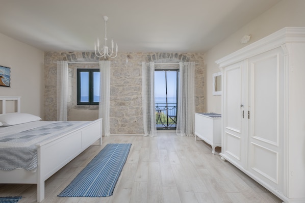 A bedroom with a bed, a wardrobe, a chandelier, and a view of the sea through a window.