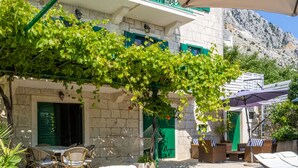 A wooden deck with lounge chairs, a pool, and a stone building with green shutters. - Last minute for June - romantic villa with pool and BBQ, 6 min from the sea (Podgora)