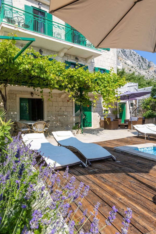 A wooden deck with lounge chairs, a pool, and a stone building with green shutters. - Last minute for June - romantic villa with pool and BBQ, 6 min from the sea (Podgora)