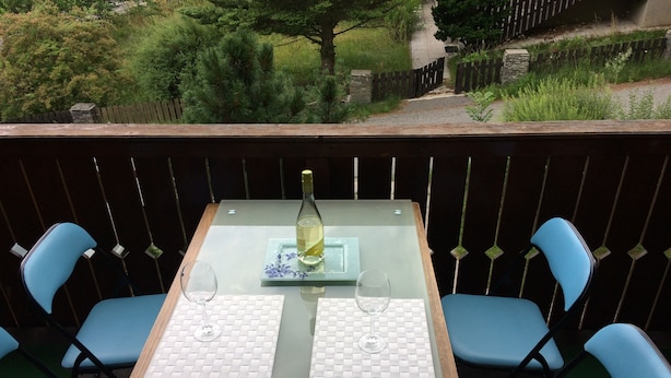 Uma área de refeições ao ar livre com uma mesa posta para dois, com uma garrafa de vinho branco e duas taças.