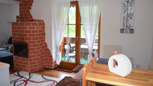 Uma sala de estar acolhedora com lareira de tijolos, uma mesa de madeira e vista para o exterior através de uma porta de vidro.