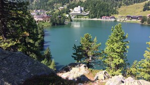 Um lago rodeado por montanhas, com um edifício com várias varandas com vista para a água.
