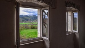Een kamer met een groot raam, dat uitzicht biedt op een groen veld en heuvels in de verte.