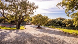 Une allée de gravier mène à un bâtiment, et on aperçoit à l’arrière-plan un terrain de tennis entouré d’une clôture.
