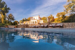 Une piscine dont l’eau reflète un bâtiment, des chaises longues et un mur de pierre.