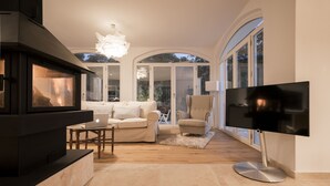 Un salon moderne avec une cheminée, un canapé, un fauteuil, un téléviseur et de grandes fenêtres.