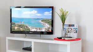 A flat-screen TV on a white entertainment unit with a remote control and decorative items. - Villa Flipa with pool Ap. Ema (Vodice)