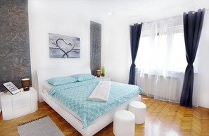 A modern bedroom with a bed, bedside tables, a nightstand, a rug, and a window with curtains.