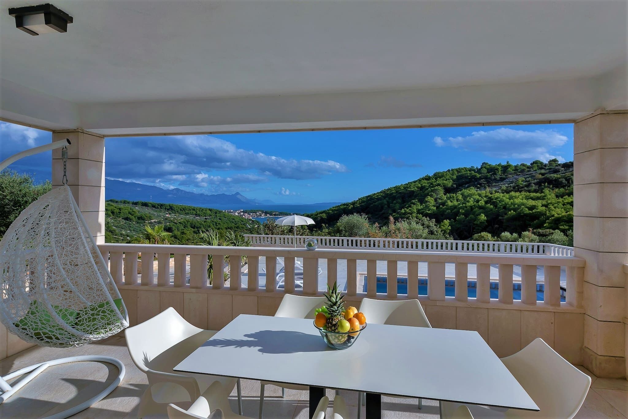 A balcony with a white table and chairs, a hanging chair, and a bowl of fruit.