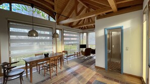 A spacious kitchen with a large dining table, wooden chairs, and a view of the outdoors through large windows.