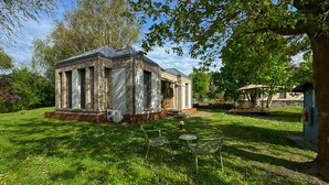 A small brick building with a covered porch, surrounded by a grassy lawn and trees.