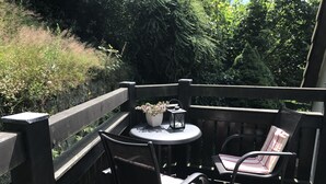 Una terraza de madera con una mesa redonda y dos sillas, rodeada por una barandilla de madera.
