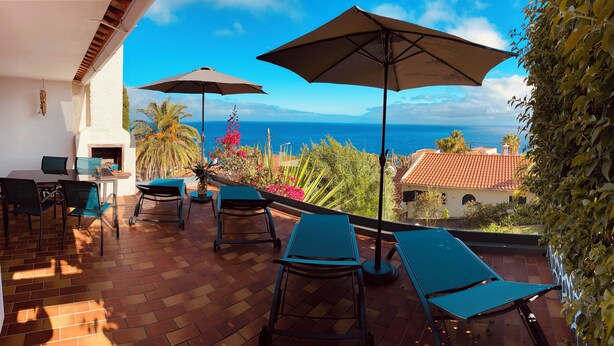 A terrace with a table and chairs, two umbrellas, and a view of the sea. - Sea view with a view  (Canico)