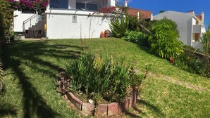 A white house with a red-tiled roof, a balcony with a black umbrella, and a well-maintained garden with various plants and a brick border. - Sea view with a view  (Canico)