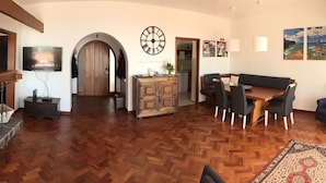 A spacious living area with a wooden herringbone floor, a dining table with chairs, a sofa, a fireplace, and a kitchen visible through an archway. - Sea view with a view  (Canico)
