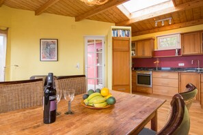 Une table de salle à manger en bois, avec une bouteille de vin, un verre et un panier de fruits.