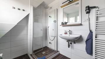 Un baño moderno con cabina de ducha de vidrio, un lavabo blanco, un perchero y un estante de madera.
