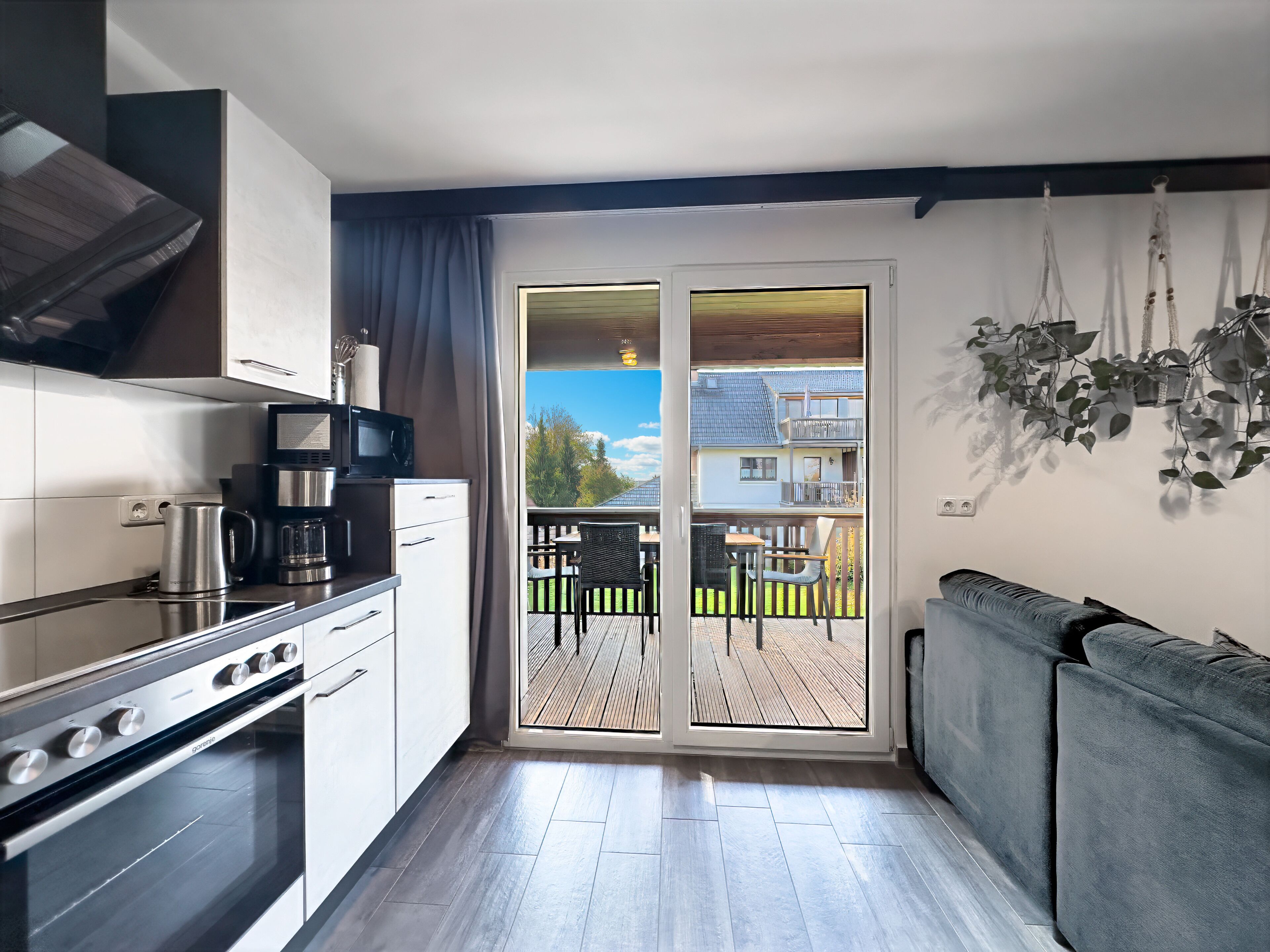 Een moderne keuken met een inbouwoven, een koffiezetapparaat en een magnetron. Er is een balkon met tuinmeubilair en uitzicht op omliggende huizen.