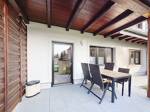 A covered patio with a table and chairs, a door leading to the interior, and a view of the outside.
