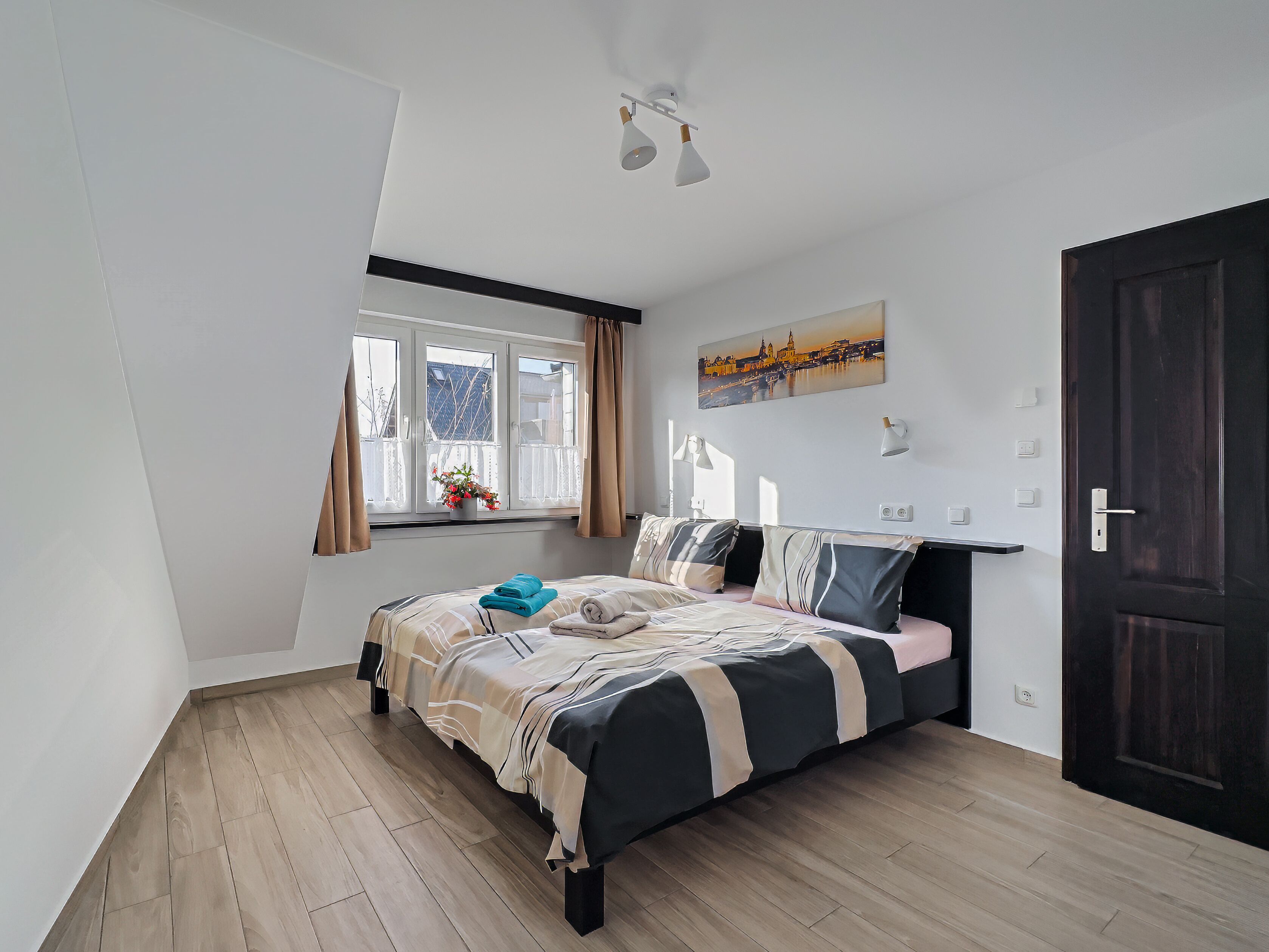 Une chambre à coucher avec un lit, une fenêtre avec des rideaux, un tableau et une porte.