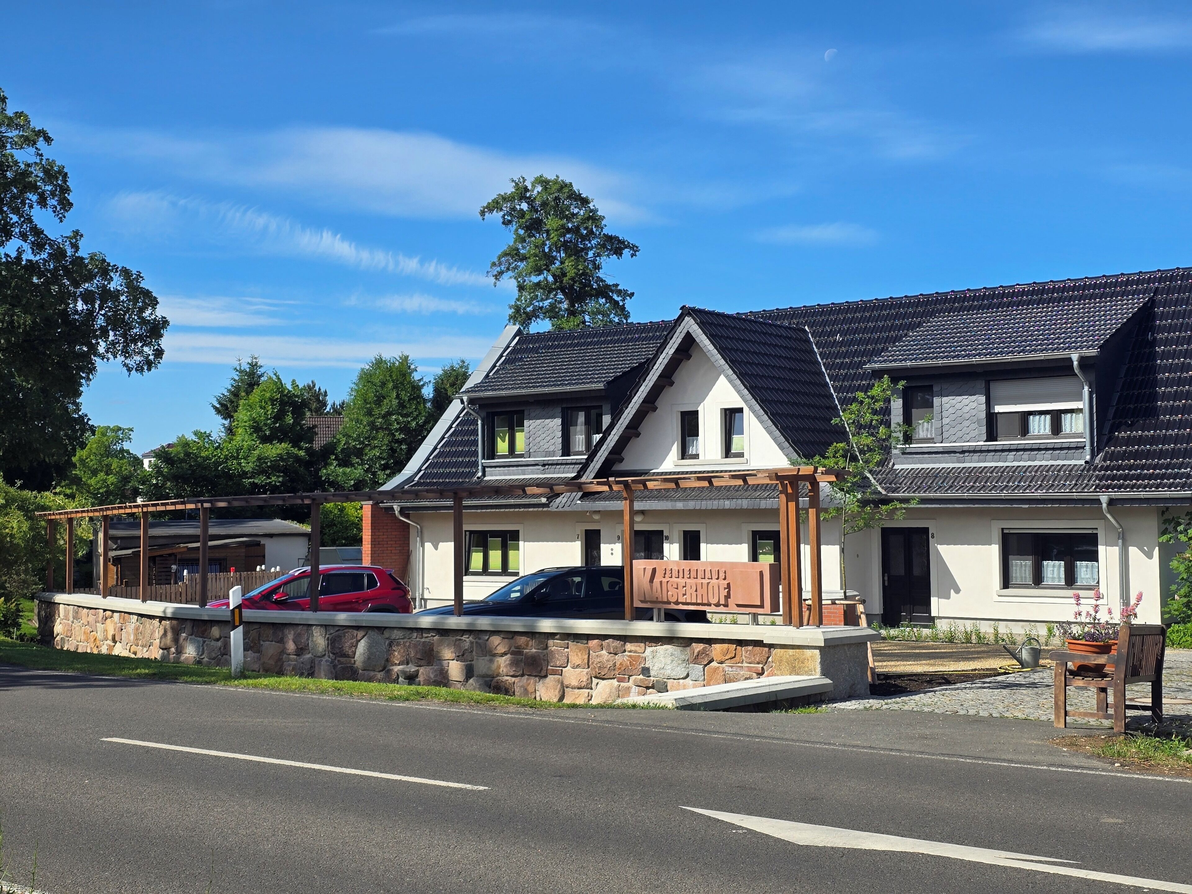 A two-story house with a stone wall, a covered porch, and a car parked in front.