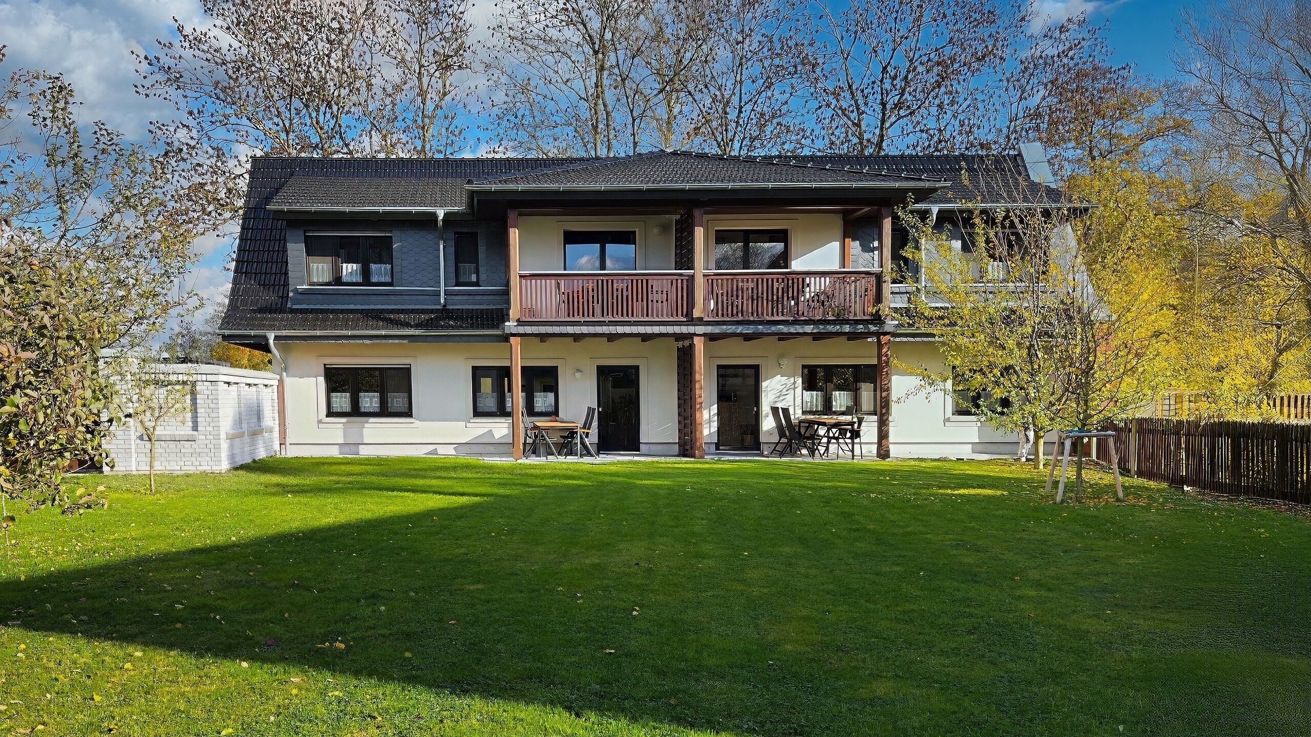 A two-story house with a balcony, a front lawn, and trees in the background.