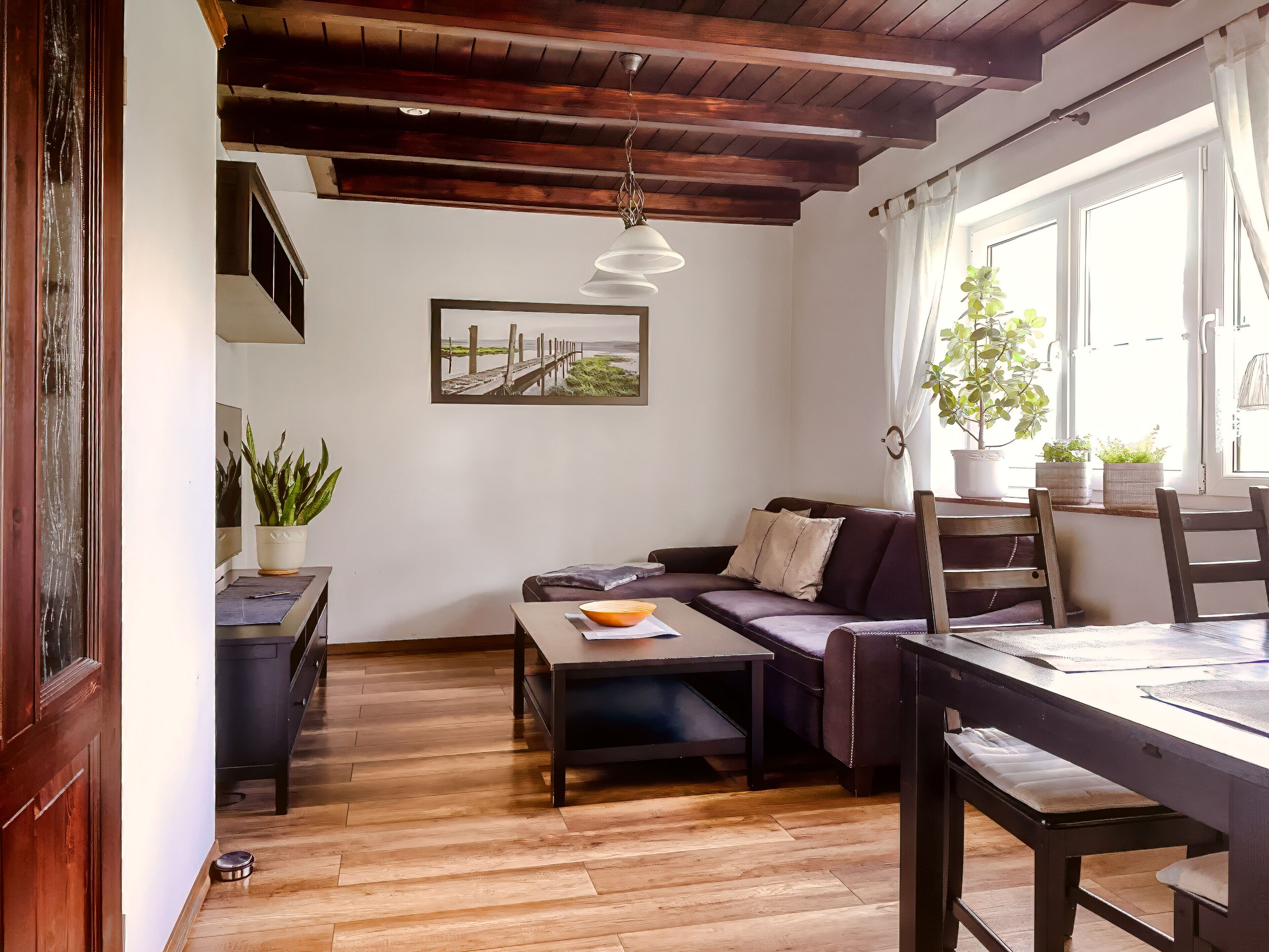 Un salon chaleureux avec un plafond en bois, un canapé, une table à manger et une fenêtre avec des rideaux.