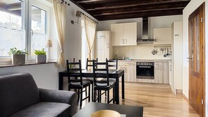 A modern kitchen with wooden cabinets, a dining area with a sofa and chairs, and a large window with curtains. - Ferienhaus Kaiserhof (Markkleeberg)