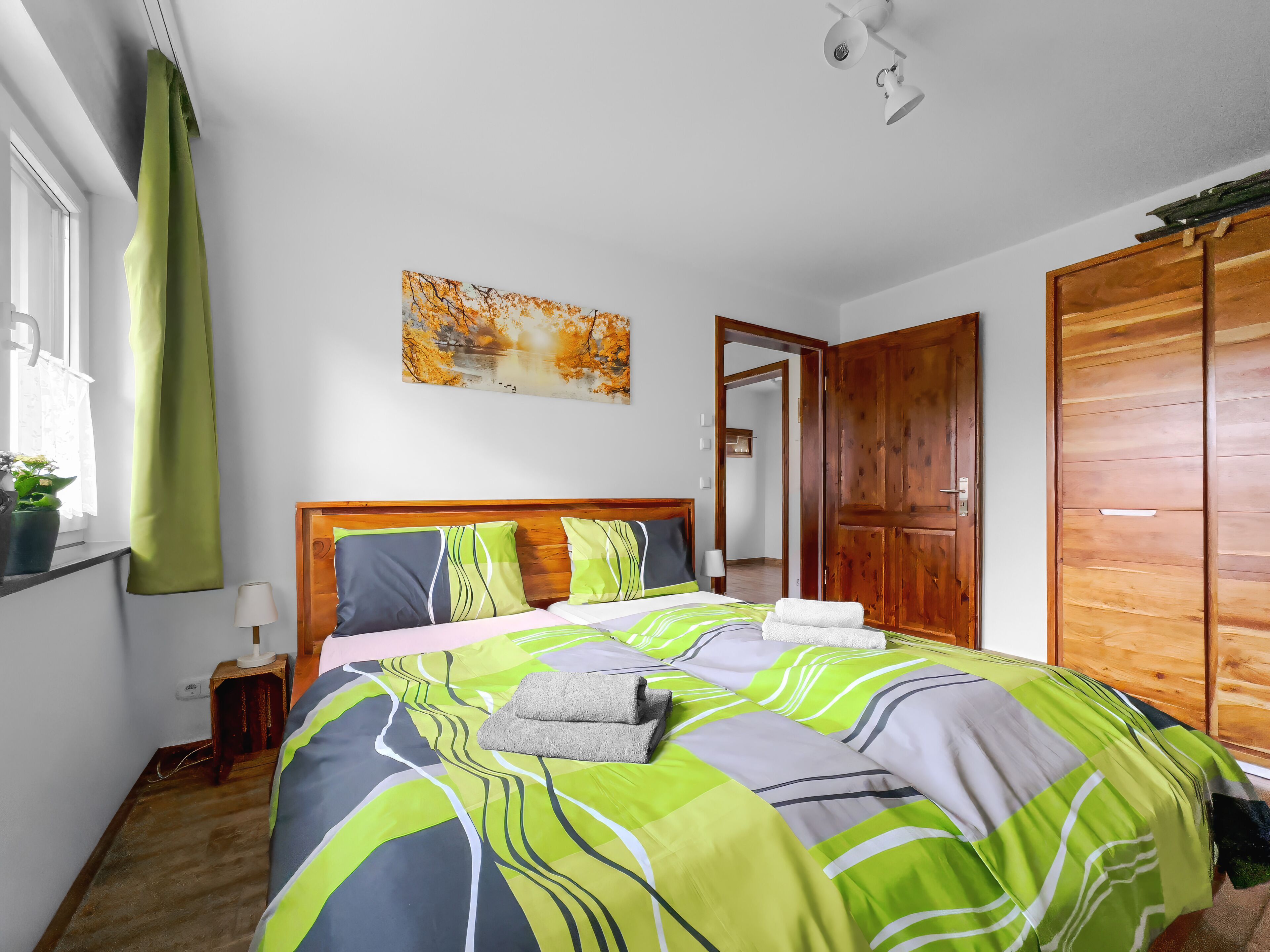Un dormitorio con cama, ventana con cortinas, un cuadro en la pared y un armario de madera.