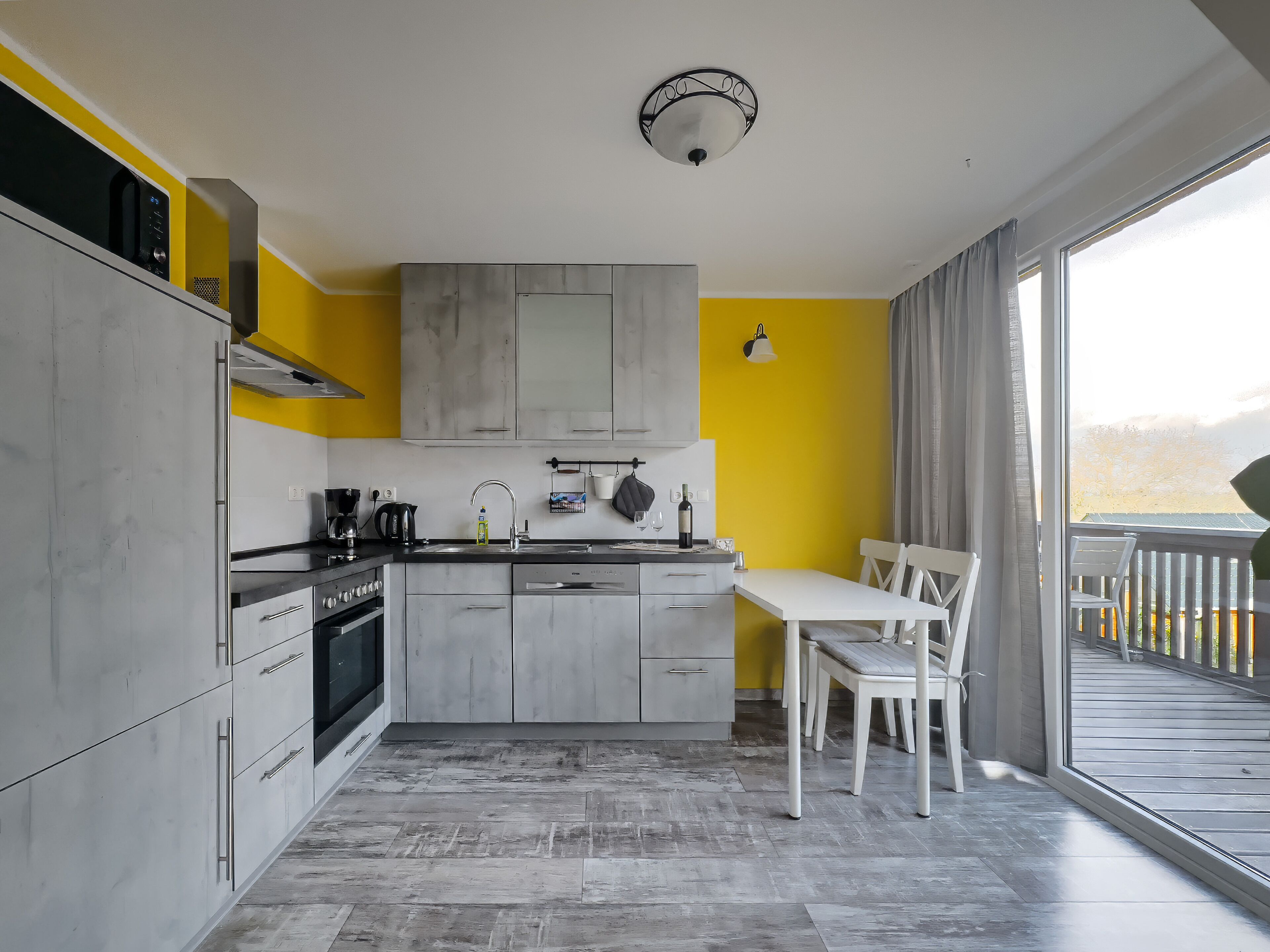 A modern kitchen with grey cabinets, a white countertop, and a dining area with a white table and chairs.