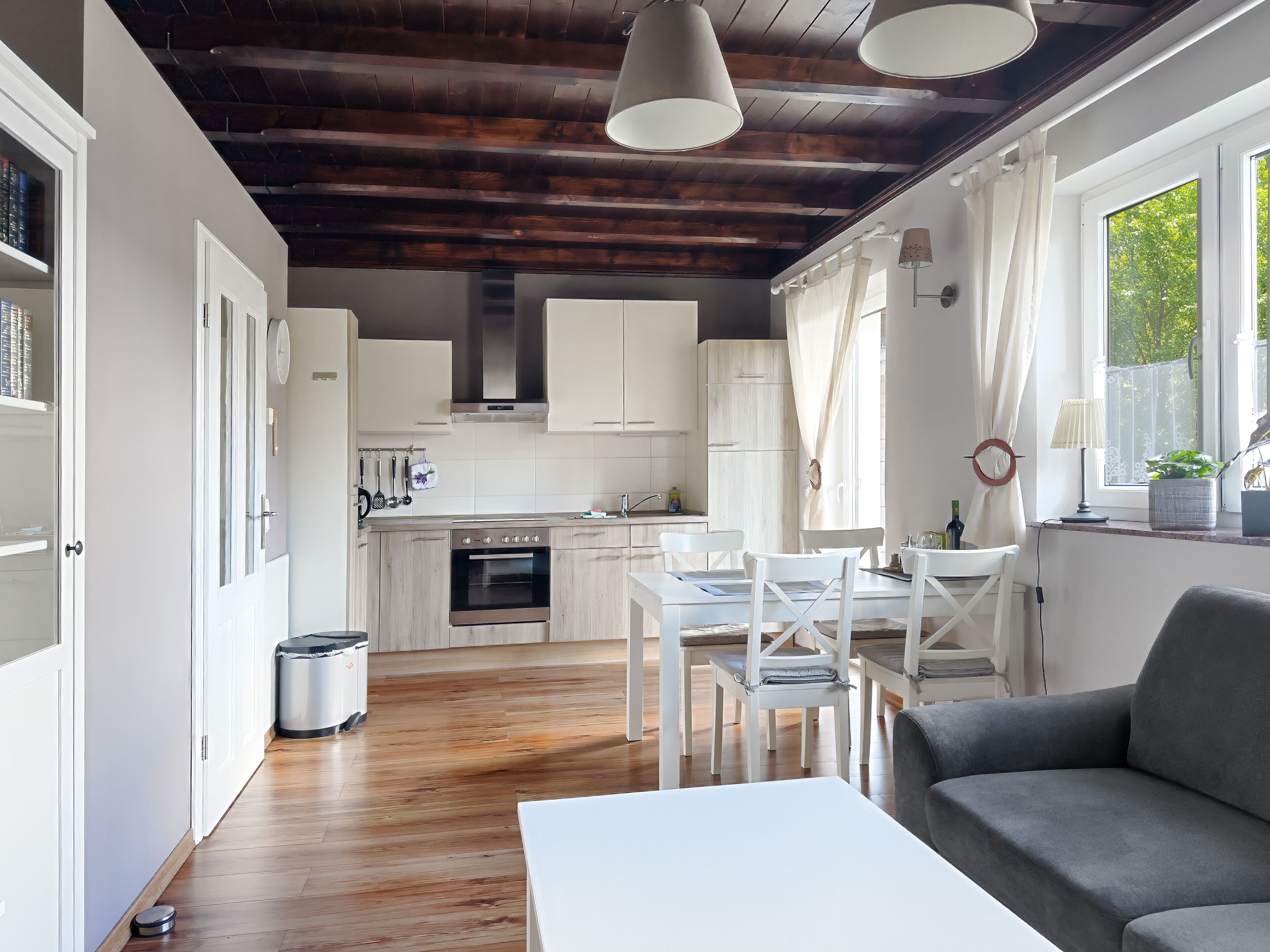 A modern kitchen with white cabinets, a built-in oven, and a dining area with a white table and chairs.
