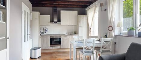 A modern kitchen with white cabinets, a built-in oven, and a dining area with a white table and chairs.