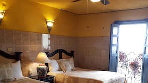 A hotel room with two beds, a nightstand with a lamp, and a view of the outside through a window. - Hotel Barranca 10 (San Miguel de Allende)