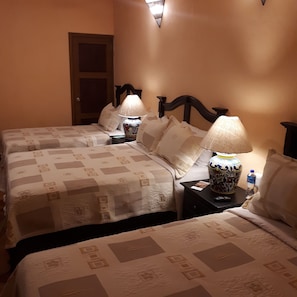Une chambre d’hôtel avec deux lits, chacun recouvert d’une couvre-lit à motifs et agrémenté de deux oreillers. Il y a deux tables de chevet, chacune équipée d’une lampe et d’une télécommande. Une bouteille d’eau est posée sur l’une des tables.