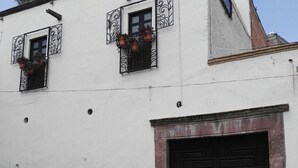 A building with two black doors, a red sign, and a window with potted plants. - Hotel Barranca 10 (San Miguel de Allende)